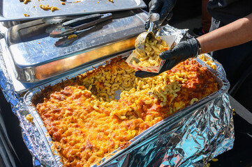 Hands Serving Jerk Chicken Mac and Cheese at the Poboy Festival on Oak Street in New Orleans, LA,...