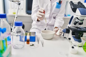 Young beautiful hispanic woman scientist pouring liquid on bowl at laboratory