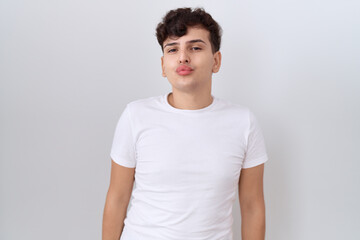 Young non binary man wearing casual white t shirt looking at the camera blowing a kiss on air being lovely and sexy. love expression.