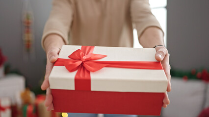 Young arab man holding gift standing by christmas tree at home