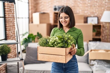 Young beautiful hispanic woman smiling confident holding wooden plant pot at new home