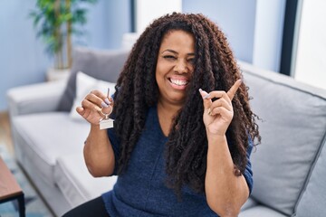 Plus size hispanic woman holding keys of new home smiling happy pointing with hand and finger to the side