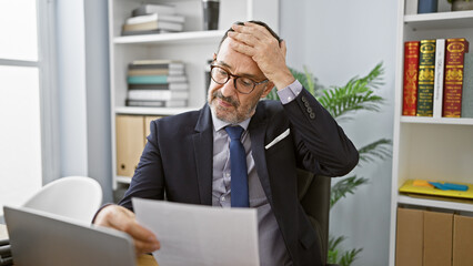 Worried grey-haired middle age man reading critical business document in office, engrossed in deep...