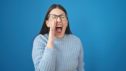 Young hispanic woman screaming loudly with hands on mouth over isolated blue background