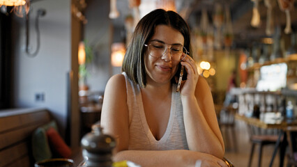 Young beautiful hispanic woman speaking on the phone sitting on the table at the restaurant