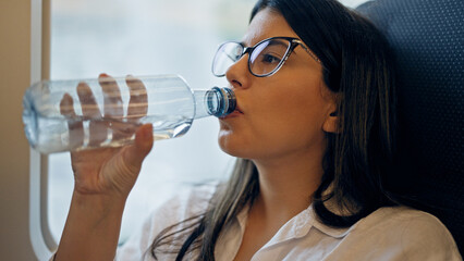 Young beautiful hispanic woman drinking water from plastic bottle inside train wagon