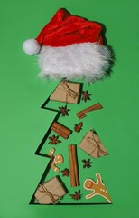 green background. Christmas tree-shaped gifts, cinnamon, anise, Christmas cookies. Santa Claus hat in the shape of a Christmas tree.