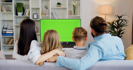 Couple sitting together on couch at home, watching tv shows with chroma-key green screen. Wife and husband resting at home together. Green screen. Chromakey. Home theater.