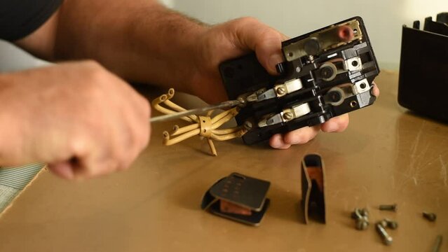 The electrician uses a screwdriver to unscrew the bolt from the switch terminal and remove the old wires.