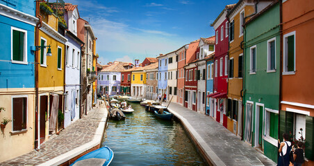 Village of Burano, Italy with colorful houses and boats lining the canal on a perfect blue sky day.
