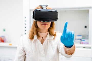 Portrait of young scientist in VR glasses moves finger imitating touch. Curious blonde woman in...