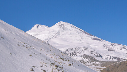 Fototapeta na wymiar The white peaks of the highest mountain in Europe. The snow-capped peak of Mount Elbrus. Vacation at a ski resort. Rest in the mountains. Sleeping volcano Elbrus. The conquest of the mountains.