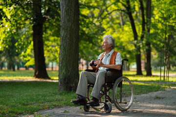 Senior man in wheelchair spending free time outdoors in nature, watching forest animals through...