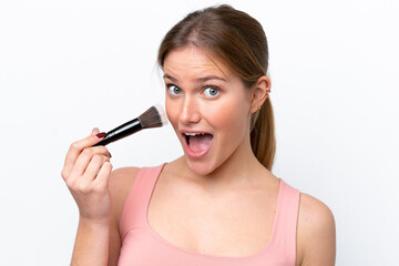 Young caucasian woman isolated on white background holding makeup brush and surprised