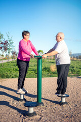 Retired male and female couple performing gymnastic exercises on a street simulator. Healthy...