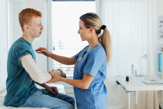 Doctor checking the orthopedic cast, brace on a teenage patient's broken arm. Teenage boy is healing a fracture after an accident.
