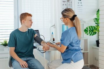 Doctor measuring boy's blood pressure, using blood pressure monitor. Teenage boy visiting...