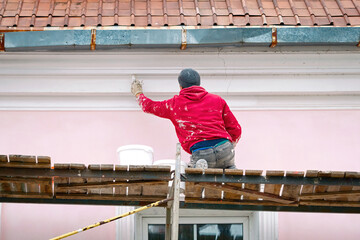 Worker on scaffolding paint facade wall of historic building. Manual worker renew building facade....