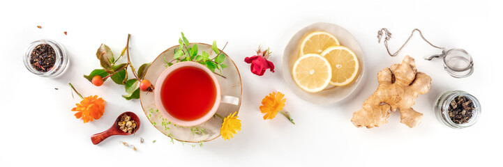 Tea with herbs, fruits, and flowers panorama, overhead flat lay shot on a white background. Healthy...