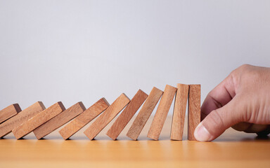 Businessman hand stopping falling blocks on table, stopping the domino effect concept for business...