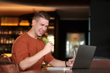 Excited young man reading e-mail with good news when sitting at table in restaurant