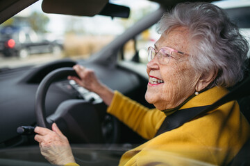 Happy senior woman driving car alone, enjoying car ride. Safe driving for elderly adults, older...