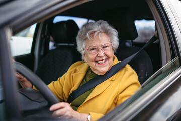 Happy senior woman driving car alone, enjoying car ride. Safe driving for elderly adults, older driver safety. - obrazy, fototapety, plakaty