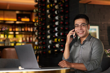 Portrait of cheerful Vietnamese entrepreneur working on laptop in his restaurant