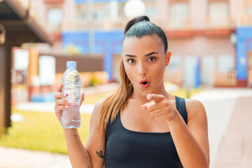 Young pretty woman with a bottle of water at outdoors surprised and pointing front