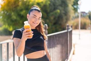 Young pretty sport woman holding an orange juice at outdoors with happy expression