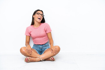 Young caucasian woman sitting on the floor isolated on white background laughing in lateral position