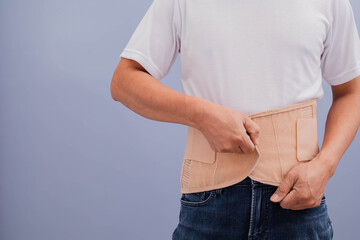 A man in a white shirt wears a waist brace to relieve back pain.