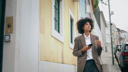 Woman using smartphone walking city street. African american girl looking phone.
