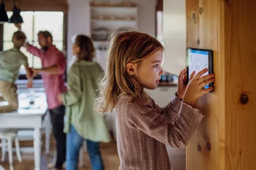 Poster Girl looking at smart thermostat at home, checking heating temperature. Concept of sustainable, efficient, and smart technology in home heating and thermostats. © Halfpoint
