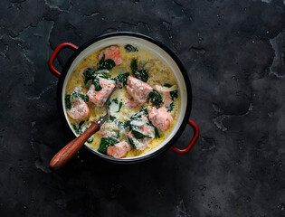 Salmon, cream, spinach sauce stew in a saucepan on a dark background, top view