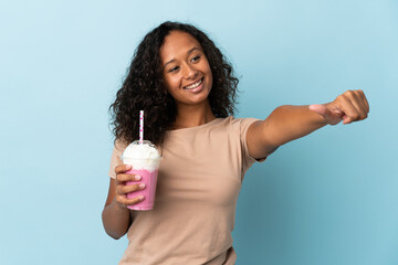 Teenager girl  with strawberry milkshake isolated on blue background giving a thumbs up gesture