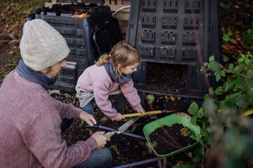 Girl helping father to remove compost from a composter in garden. Concept of composting and...