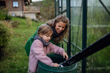 Girl and mother scooping rainwater from barell under downspout. Concept of water conservation in...