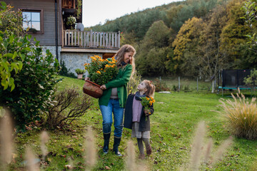 Mother and daughter taking care of home garden, replanting flowers. Pregnant mother spending time outdoors during cold autumn day.