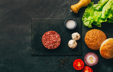 top view of hamburger ingredients raw meat buns vegetables condiments on dark table with free space for text