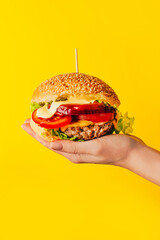 close-up of a hamburger in a woman's hand on a yellow background