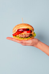 close-up of a hamburger in a woman's hand on a blue background