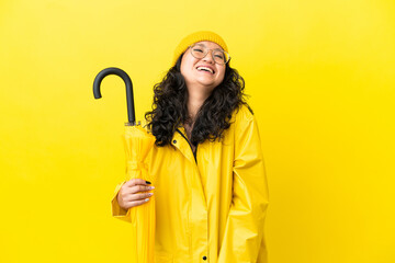 Asian woman with rainproof coat and umbrella isolated on yellow background laughing