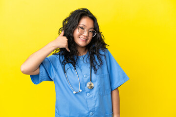 Young surgeon doctor asian woman isolated on yellow background making phone gesture. Call me back sign