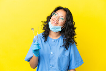 Young asian dentist holding tools over isolated background thinking an idea while looking up