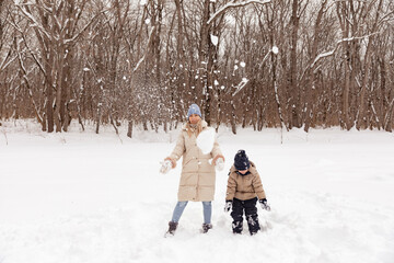 Fototapeta na wymiar Portrait of young woman with her adorable little toddler boy on a winter cold day. Mother and child tossing snow up in frosty winter park wearing stylish warm clothes and having fun outdoors.