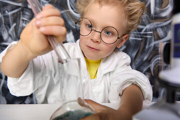 Boy mixes substances different colors in cones different shapes. Cute blond boy participates in...