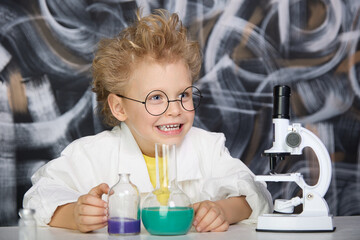 Happy child with glasses holds samples of chemical liquid in a flask with laboratory utensils on a...