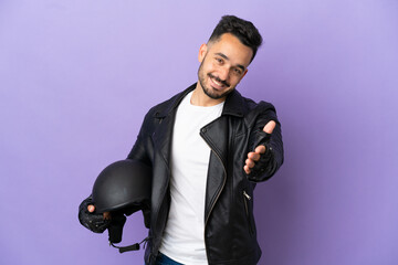Young man with a motorcycle helmet isolated on purple background shaking hands for closing a good...