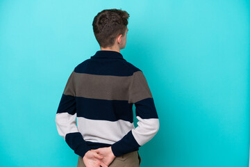 Teenager Russian man isolated on blue background in back position and looking back